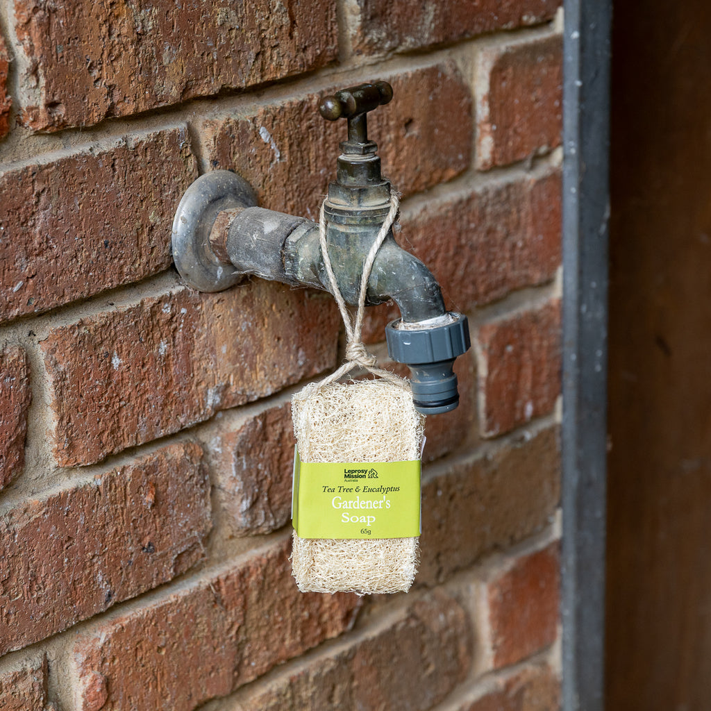 A hanging sachet of The Plant & Gardener Garden's Secrets Seeds on a rustic outdoor garden tap against a red brick wall.