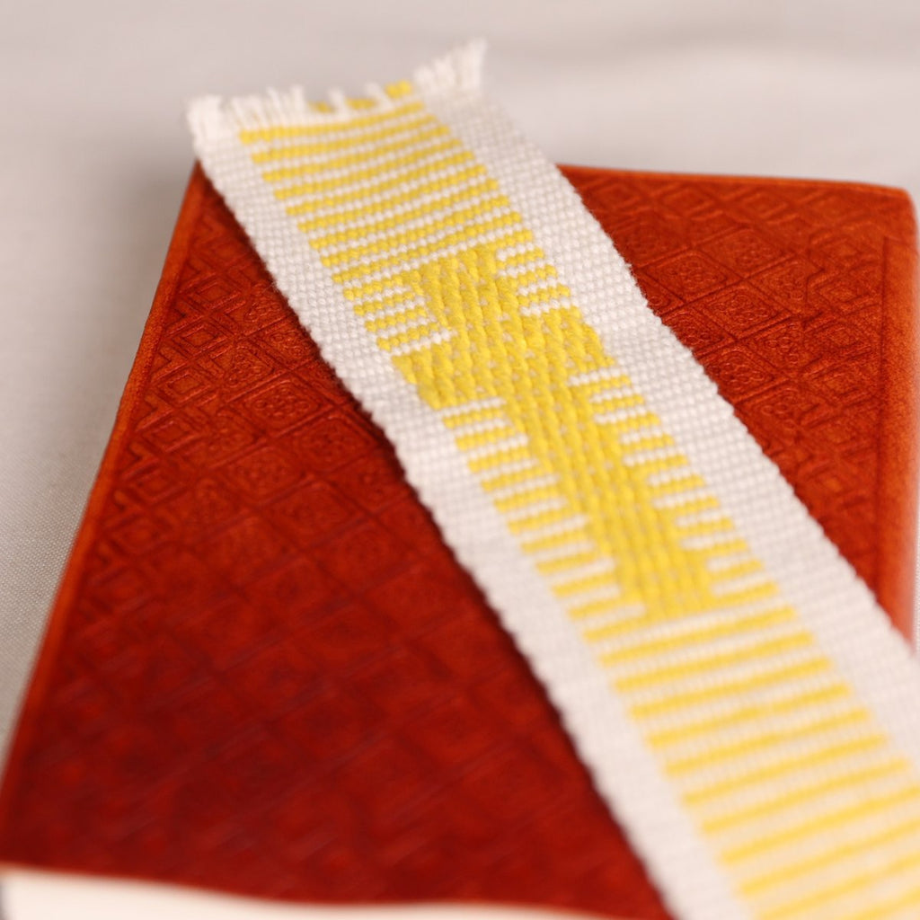 A close-up of a textured red-orange fabric or leather item with a white woven ribbon featuring a yellow geometric pattern draped diagonally across it.