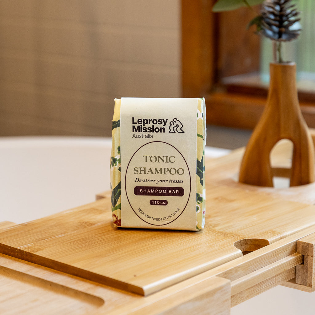 A package of Leprosy Mission Australia Tonic Shampoo bar standing on a wooden tray in a softly lit indoor setting.