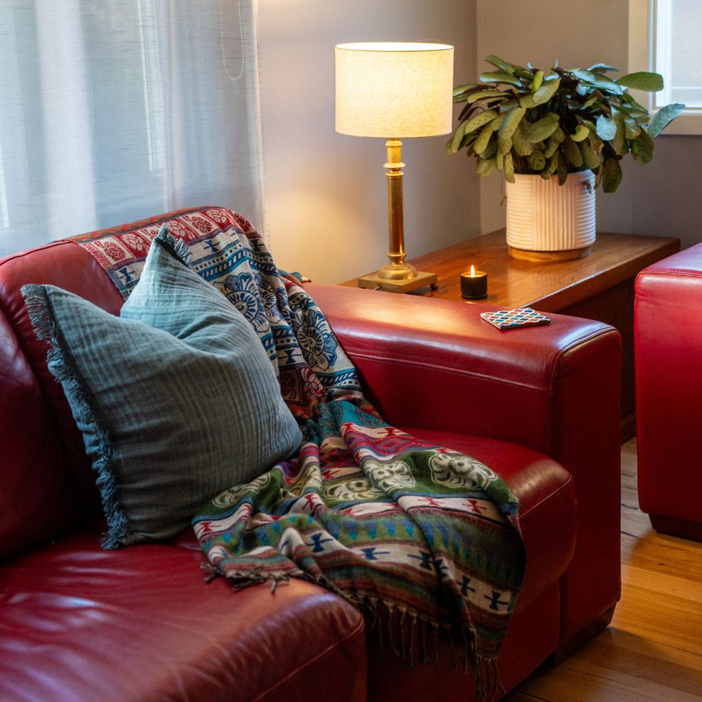 Red couch with patterned blanket and pillows in a cozy living room setting.