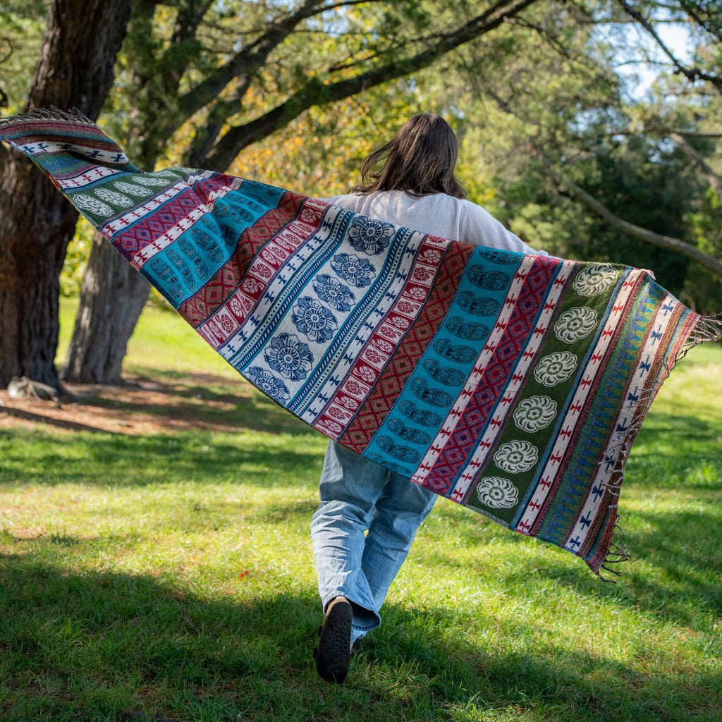 Person walking outdoors with a colorful patterned blanket draped over their shoulders