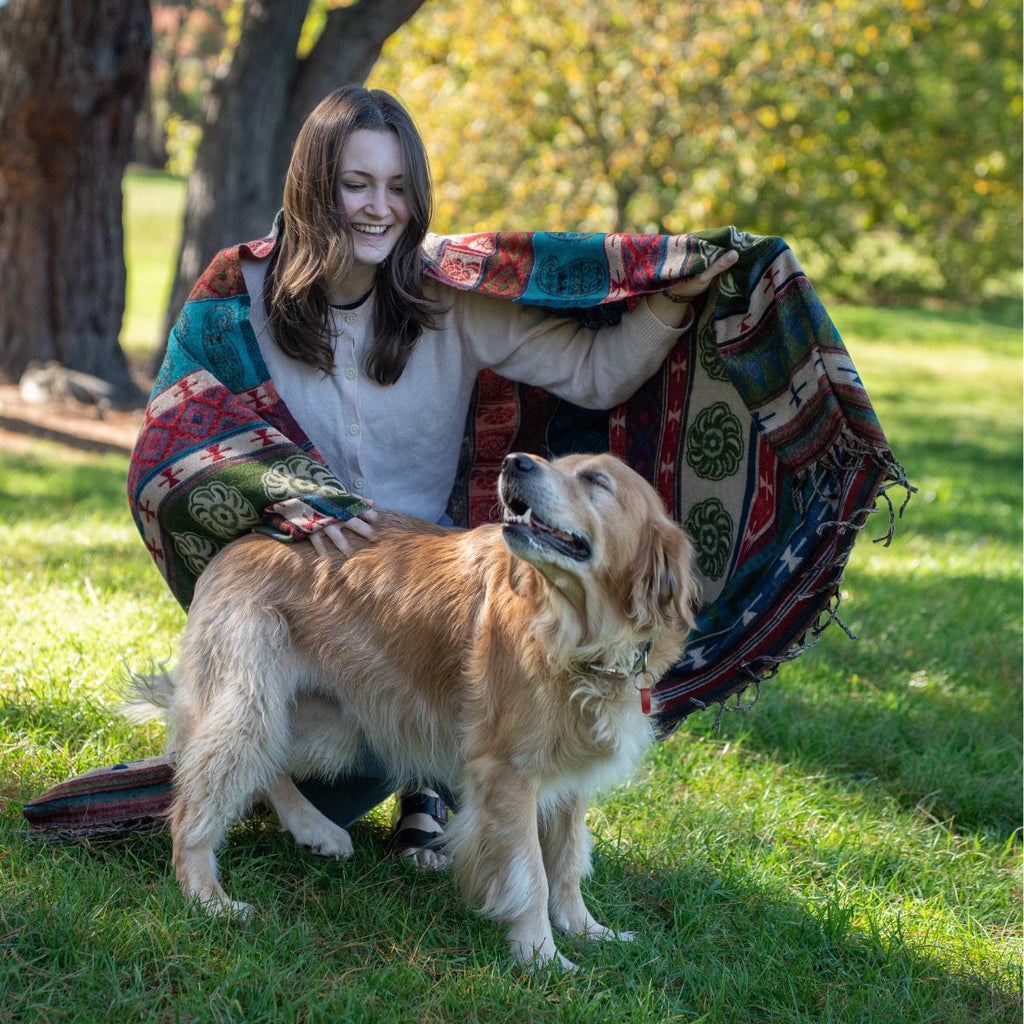 Woman sitting on the grass with a dog, wrapped in a colorful blanket