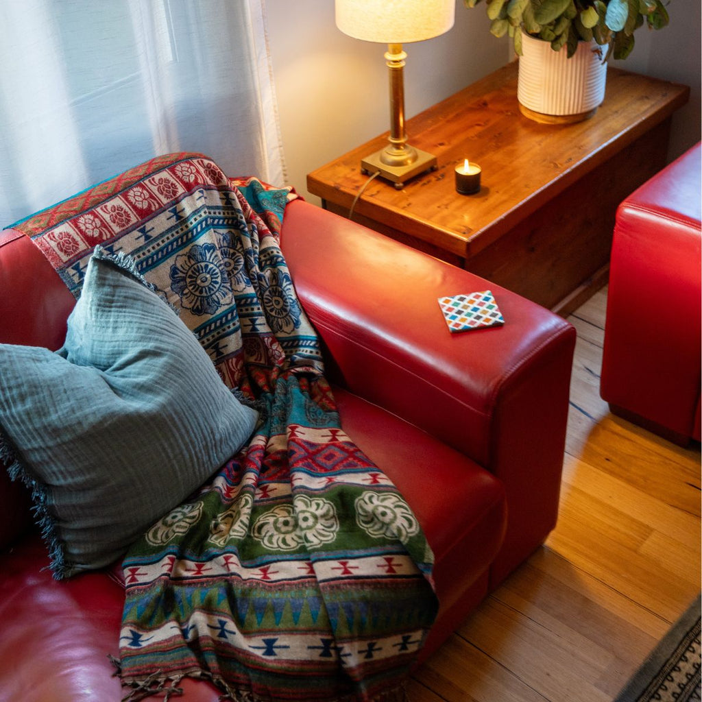 Red sofa with patterned blanket and blue pillow in a cozy living room setting.