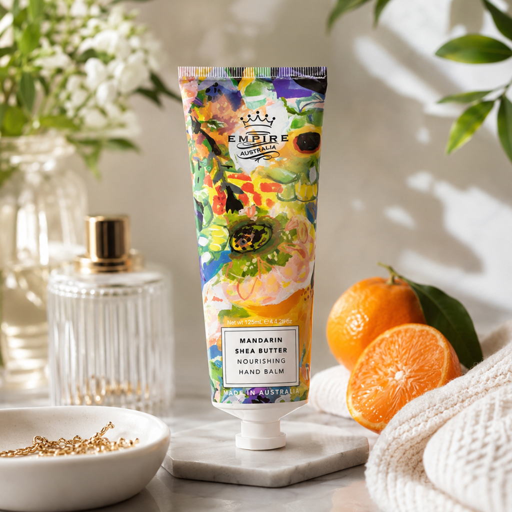 Tube of Empire Australian Mandarin Shea Butter hand balm on a marble surface with oranges and flowers.