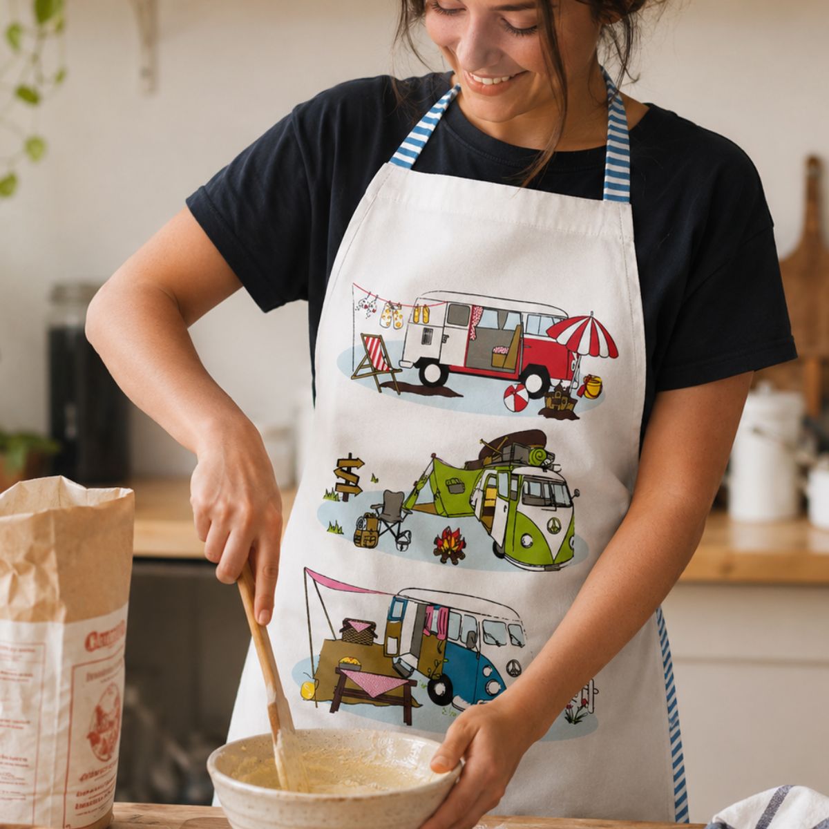 Person in a kitchen wearing an apron with camper designs, stirring a bowl.