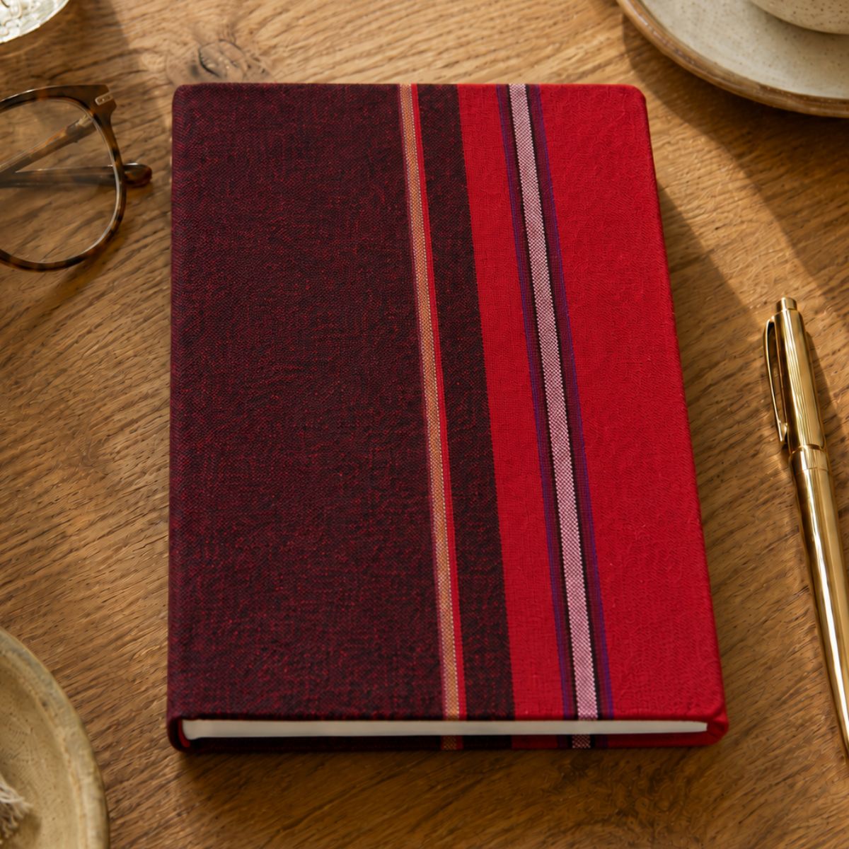 Red and purple striped notebook on a wooden table with glasses and a pen.