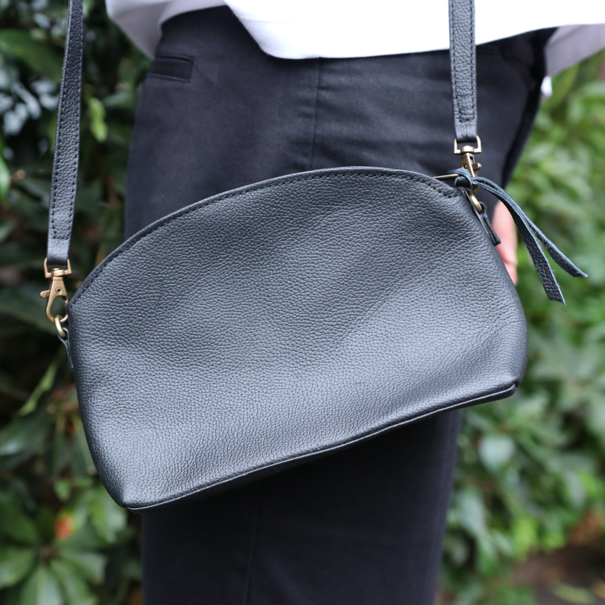 Black leather handbag held by a person with a blurred green background