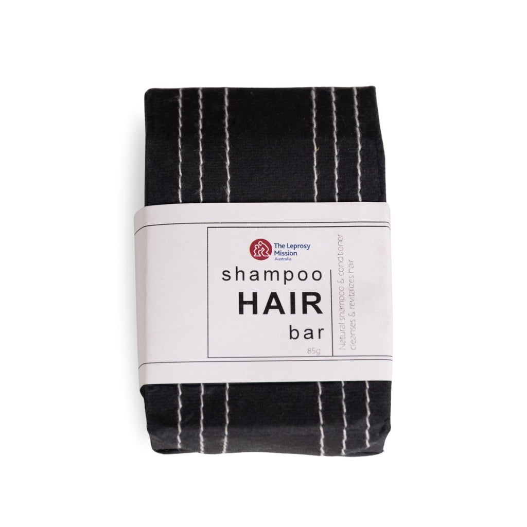 A packaged shampoo hair bar wrapped in a white paper band with the text 'shampoo HAIR bar' and a small red logo, photographed on a plain white background.