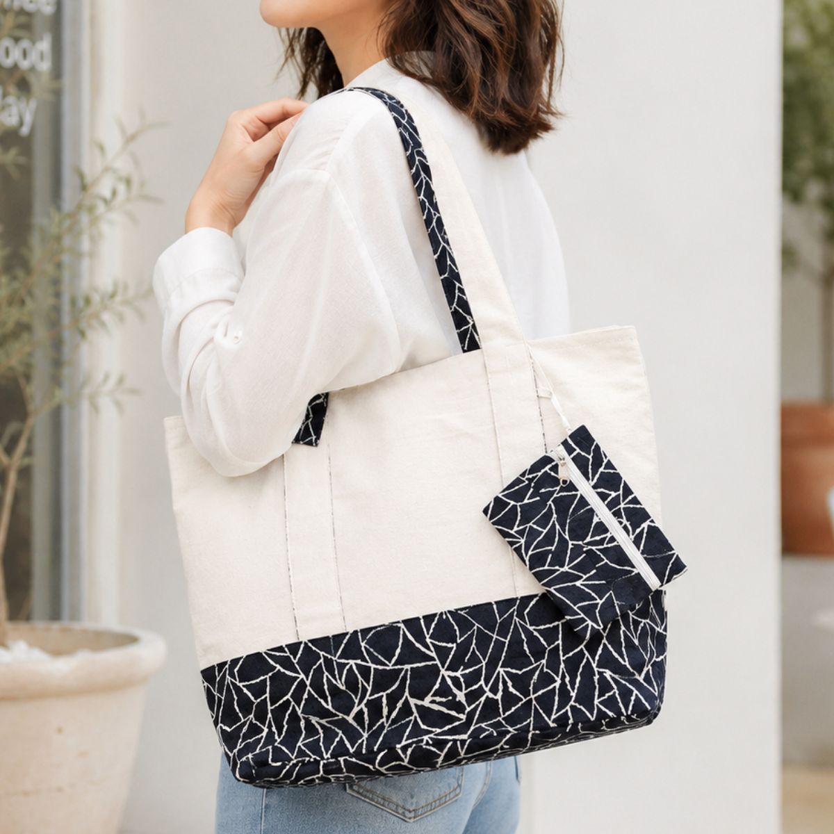 Person holding a white tote bag with black geometric pattern