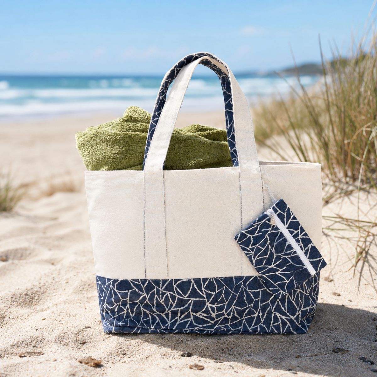Beige tote bag with blue patterned base and handle on sandy beach with green towel
