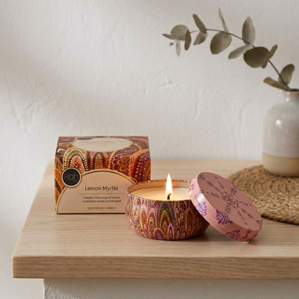 Decorative candle with colorful packaging on a wooden surface, with a plant in the background.