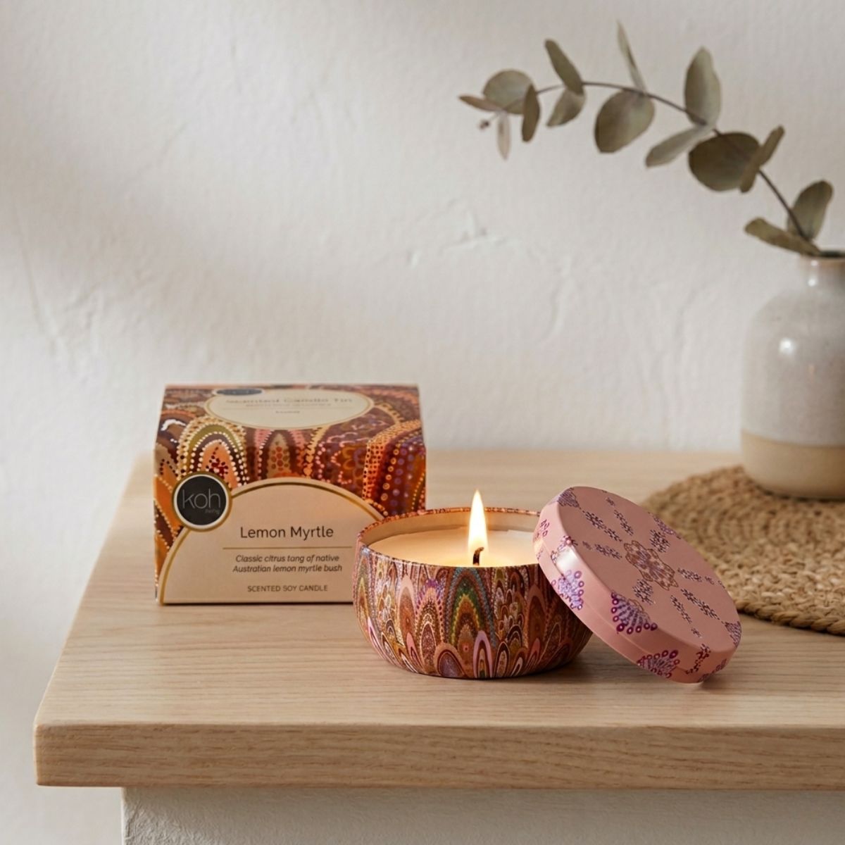 Decorative candle with colorful packaging on a wooden surface, with a plant in the background.