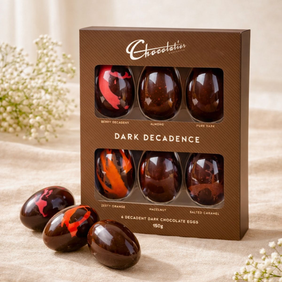 Box of Chocolatier's Dark Decadence chocolate eggs on a wooden surface with flowers in the background.