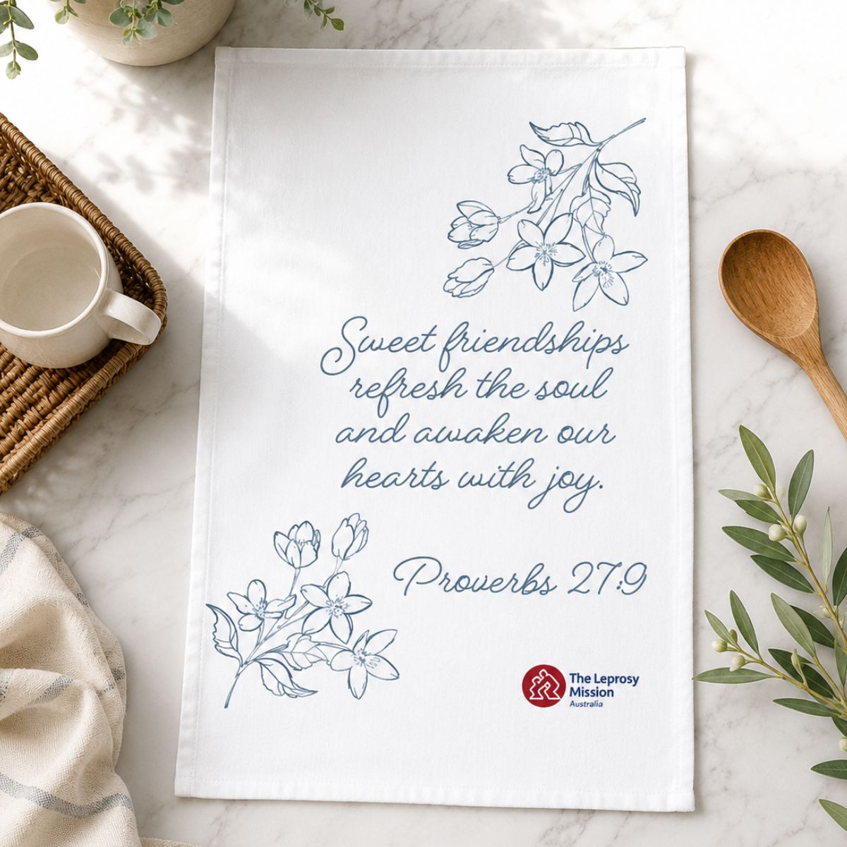 Tea towel with motivational quote and branding on a marble surface with a cup and spoon.