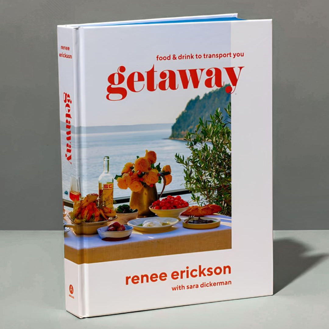 The book 'Getaway: food & drink to transport you' by Renee Erickson with Sara Dickerman, standing upright on a gray surface against a gray background. The book cover is white with a coastal scene photo and bold red title text.