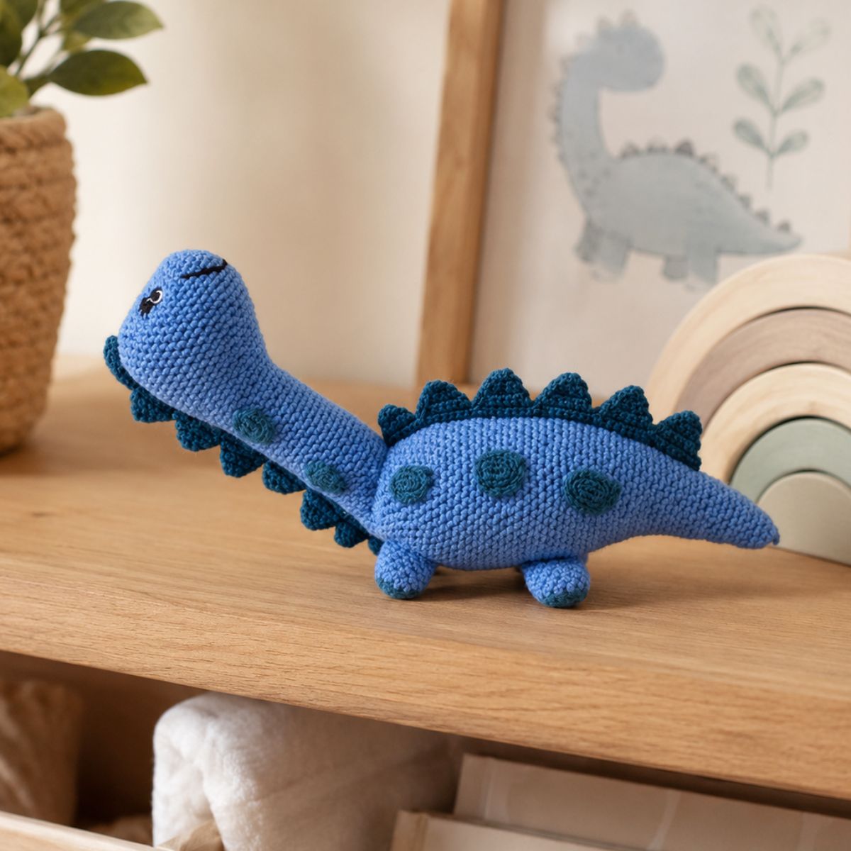 Blue crocheted dinosaur toy on a wooden surface with a soft, neutral background.