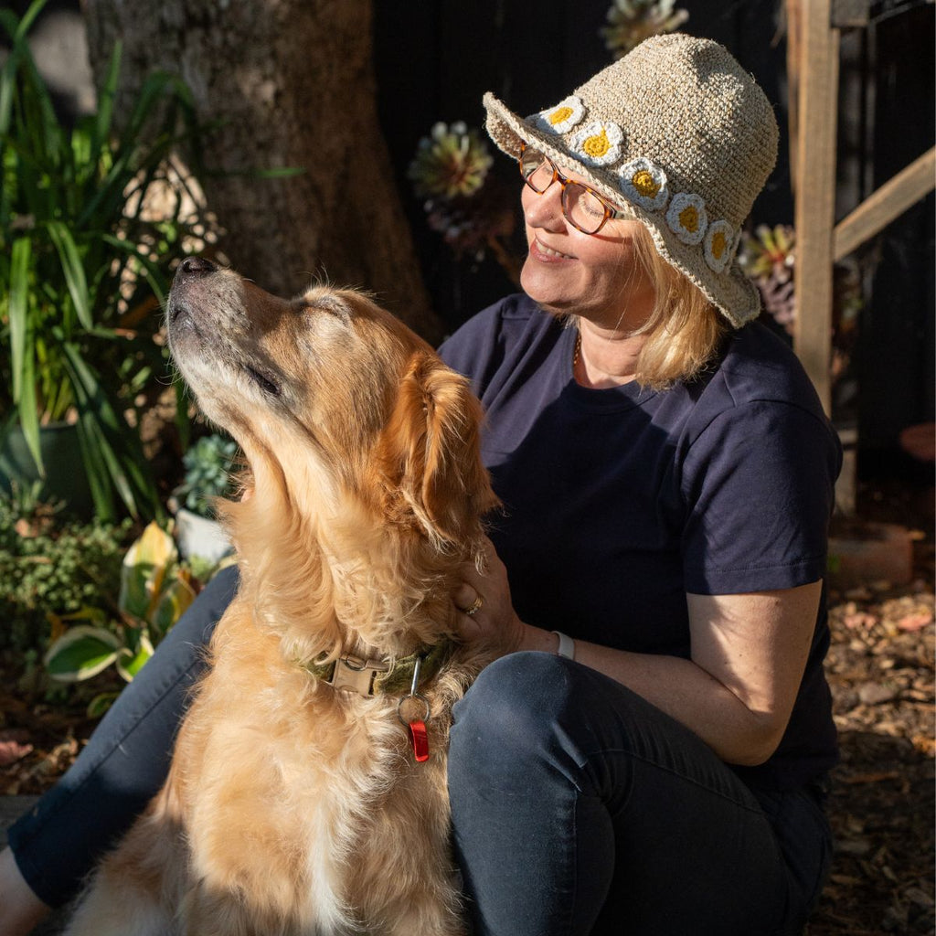 Woman wearing a sun hat with flower patterns sitting outdoors with a dog.