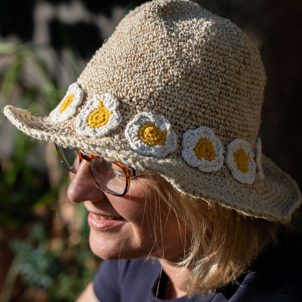 Woman wearing a crochet hat with daisy flowers and glasses, outdoors.