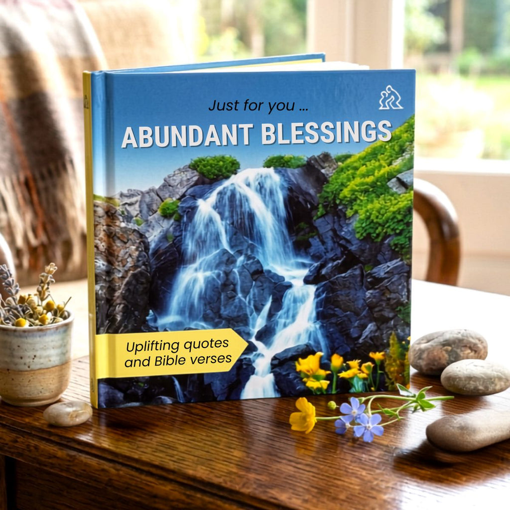 Book titled 'Abundant Blessings' with a waterfall image on a wooden surface with flowers and stones.