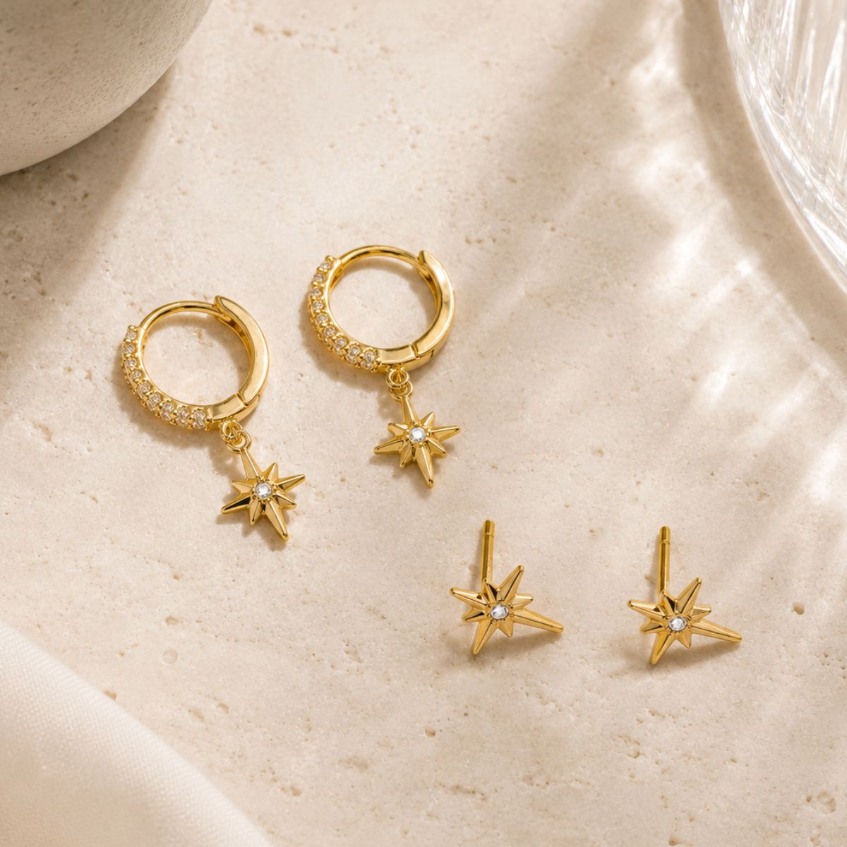 Gold hoop earrings with star-shaped pendants on a beige surface