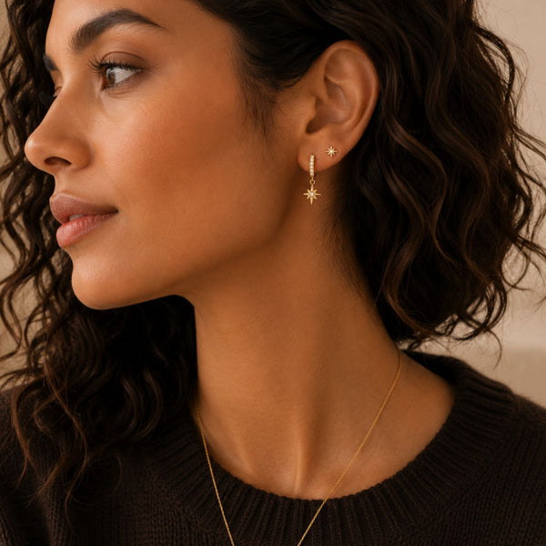 Close-up of a woman wearing gold earrings and a necklace against a neutral background