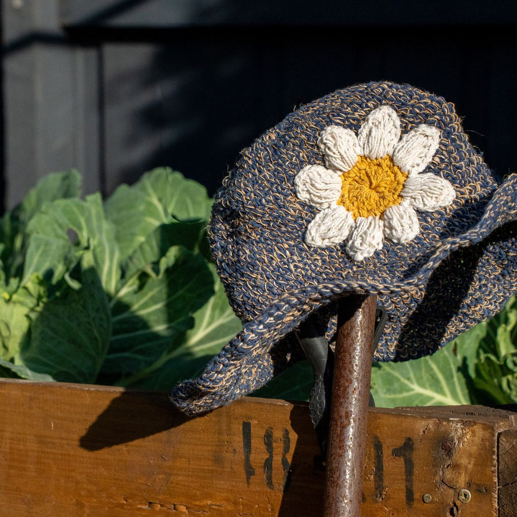 Textile flower with a daisy design on a wooden surface with plants in the background