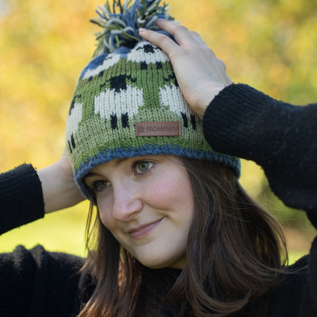 Person wearing a knitted hat with sheep pattern against a blurred natural background