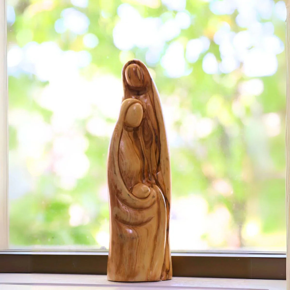 Wooden sculpture of a couple in front of a window with a blurred green outdoor background