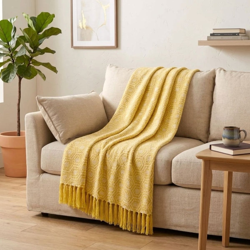Yellow blanket draped over a beige sofa in a living room setting with a plant and side table.