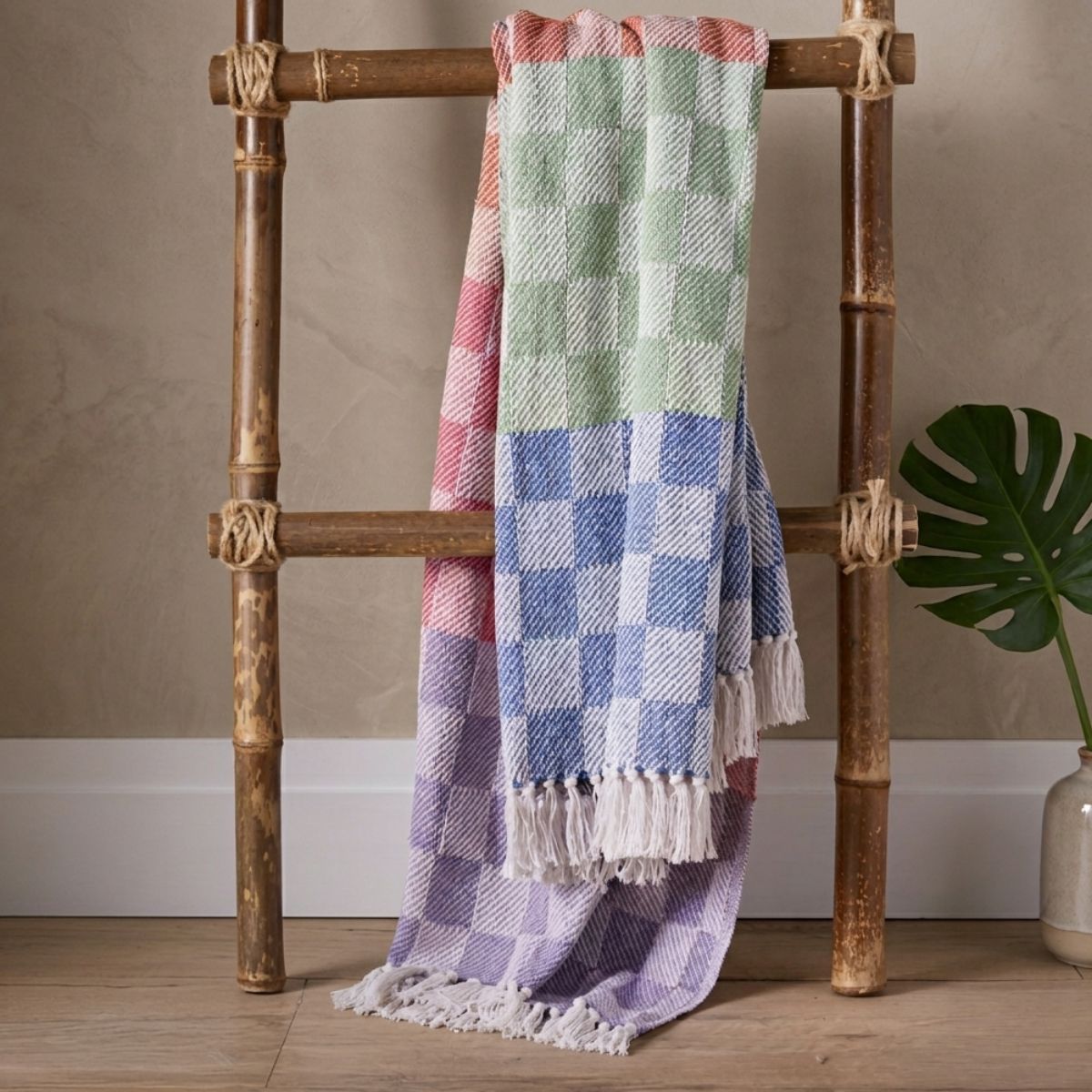 Checkered blanket draped over a wooden ladder against a neutral wall.