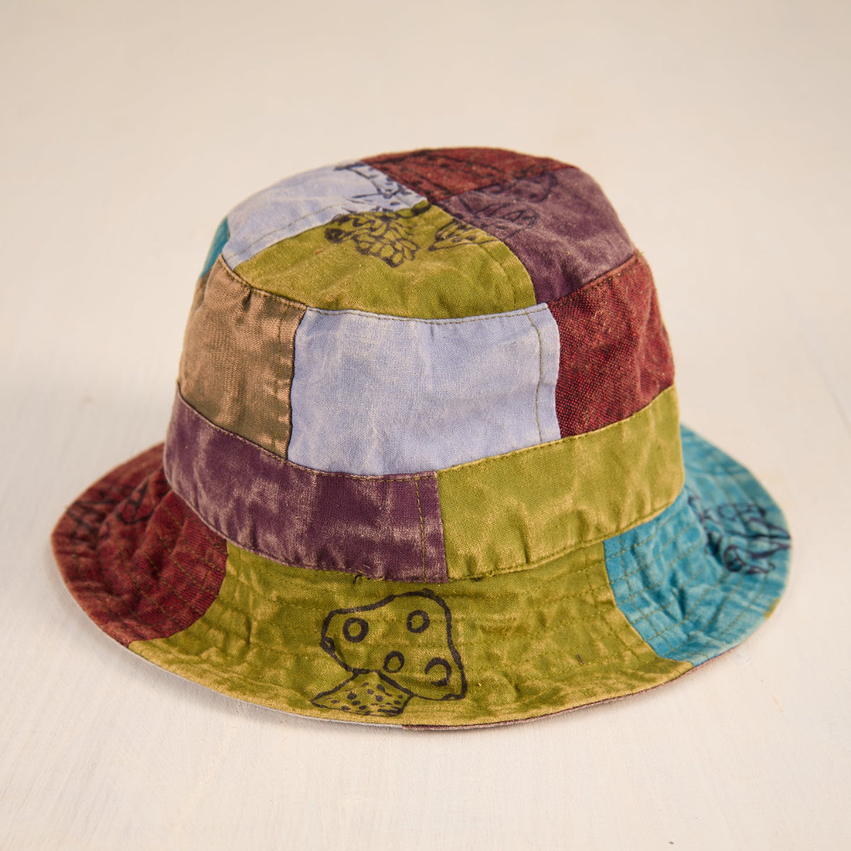 A handmade patchwork bucket hat made from various colored fabrics, featuring a stitched band and a small embroidered character on the brim, set against a plain light background.