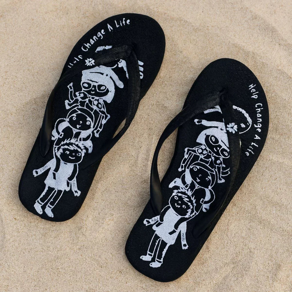 Black flip-flops with white graphics and text on a sandy background