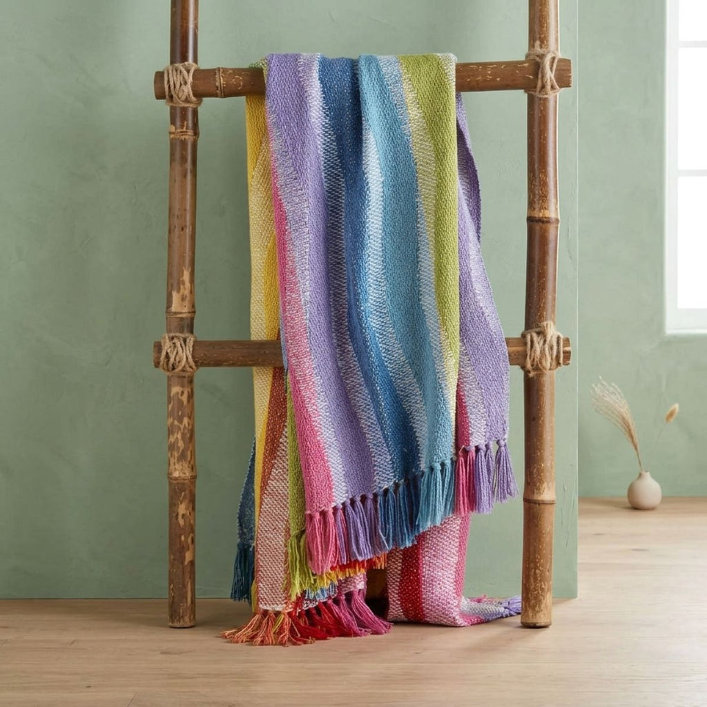 Colorful striped blanket draped over a wooden ladder against a green wall.