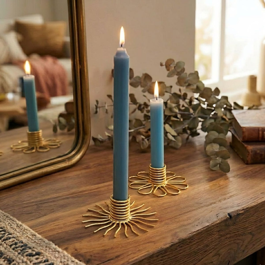 Blue candles in gold candle holders on a wooden surface with a mirror and books in the background.