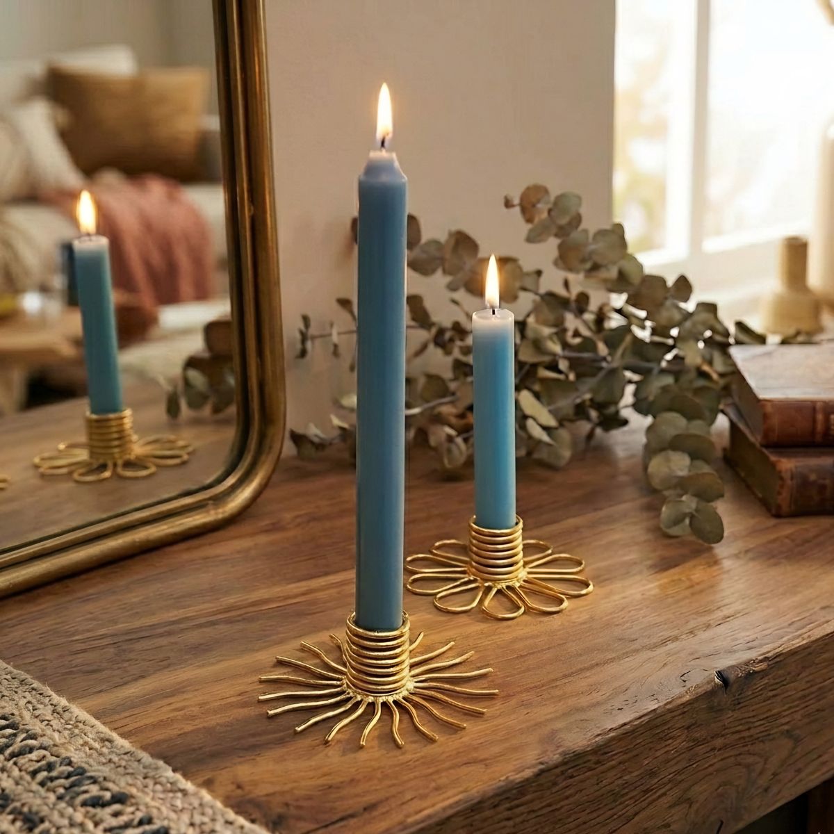 Blue candles in gold candle holders on a wooden surface with a mirror and books in the background.