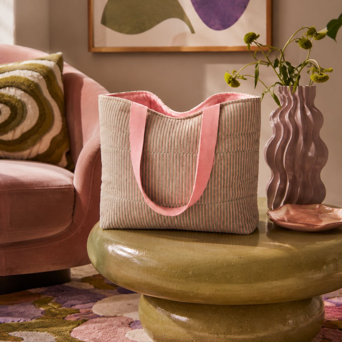 Beige tote bag with pink handles on a green table in a living room setting.