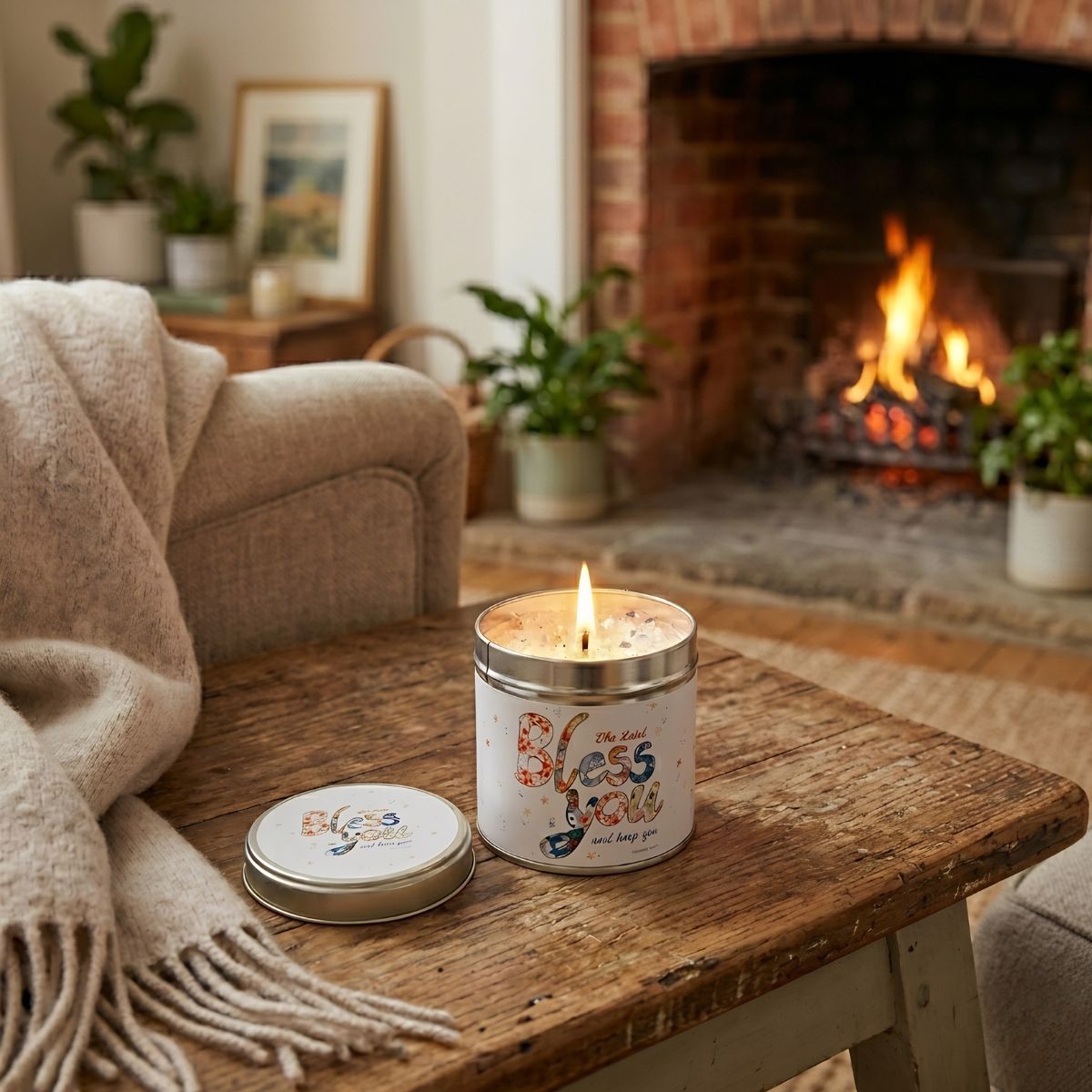 Candle in a decorative tin with 'Peace Love' text on a wooden table in a cozy living room with a fireplace.