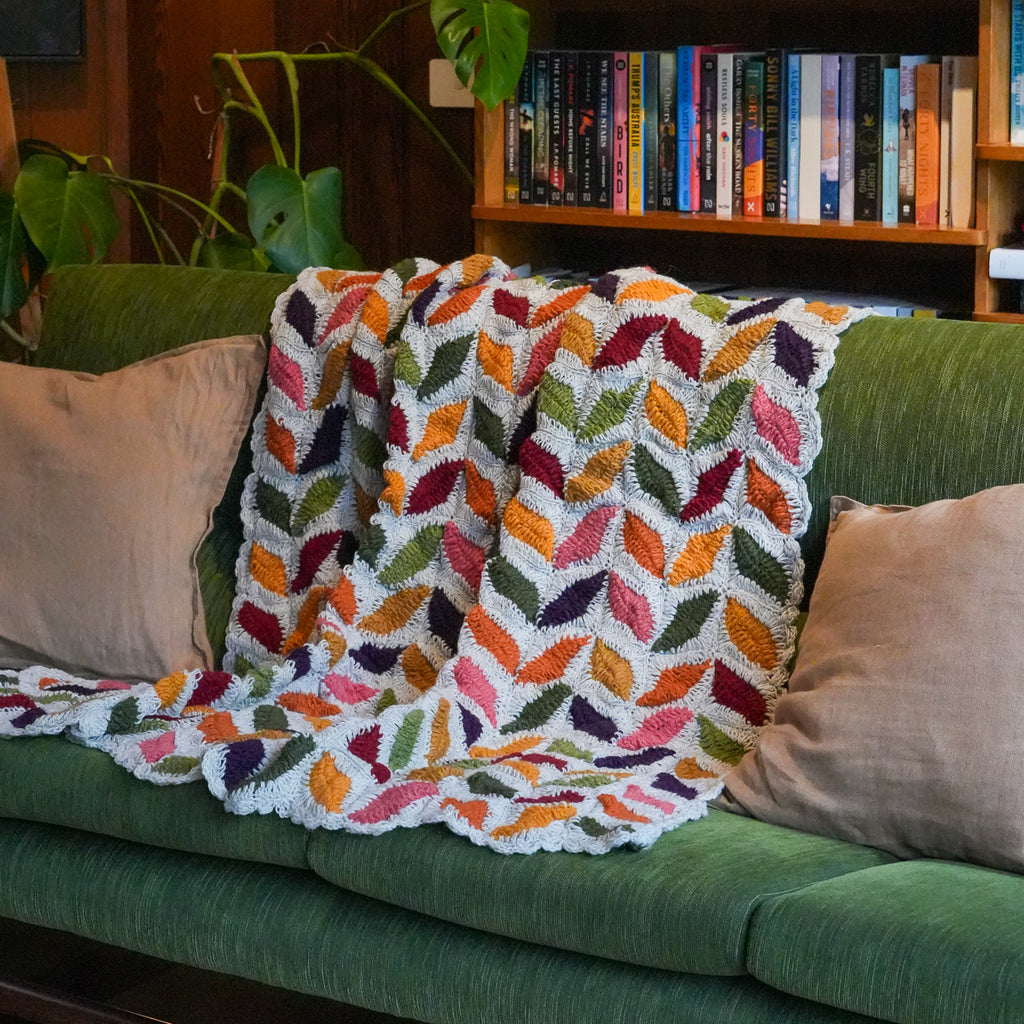 A colorful crocheted throw blanket with a leaf pattern draped over a green sofa in a cozy living room setting.