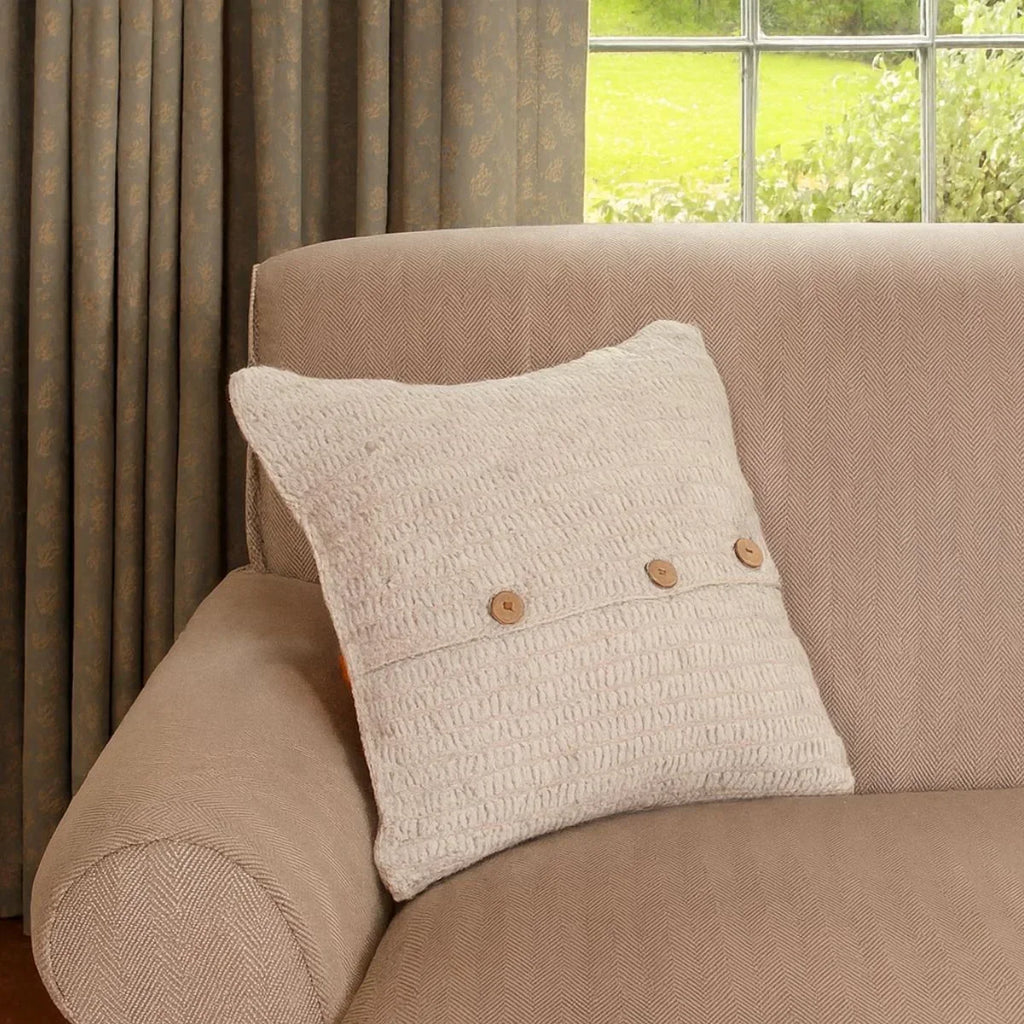 Beige pillow with wooden buttons on a beige sofa next to a window with greenery outside