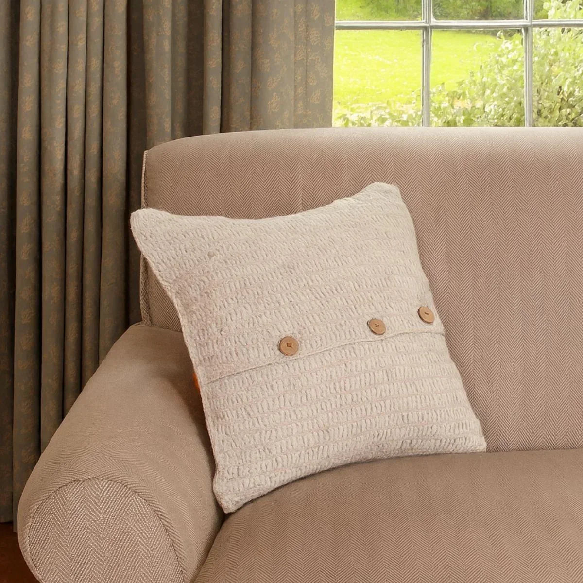 Beige pillow with wooden buttons on a beige sofa next to a window with greenery outside