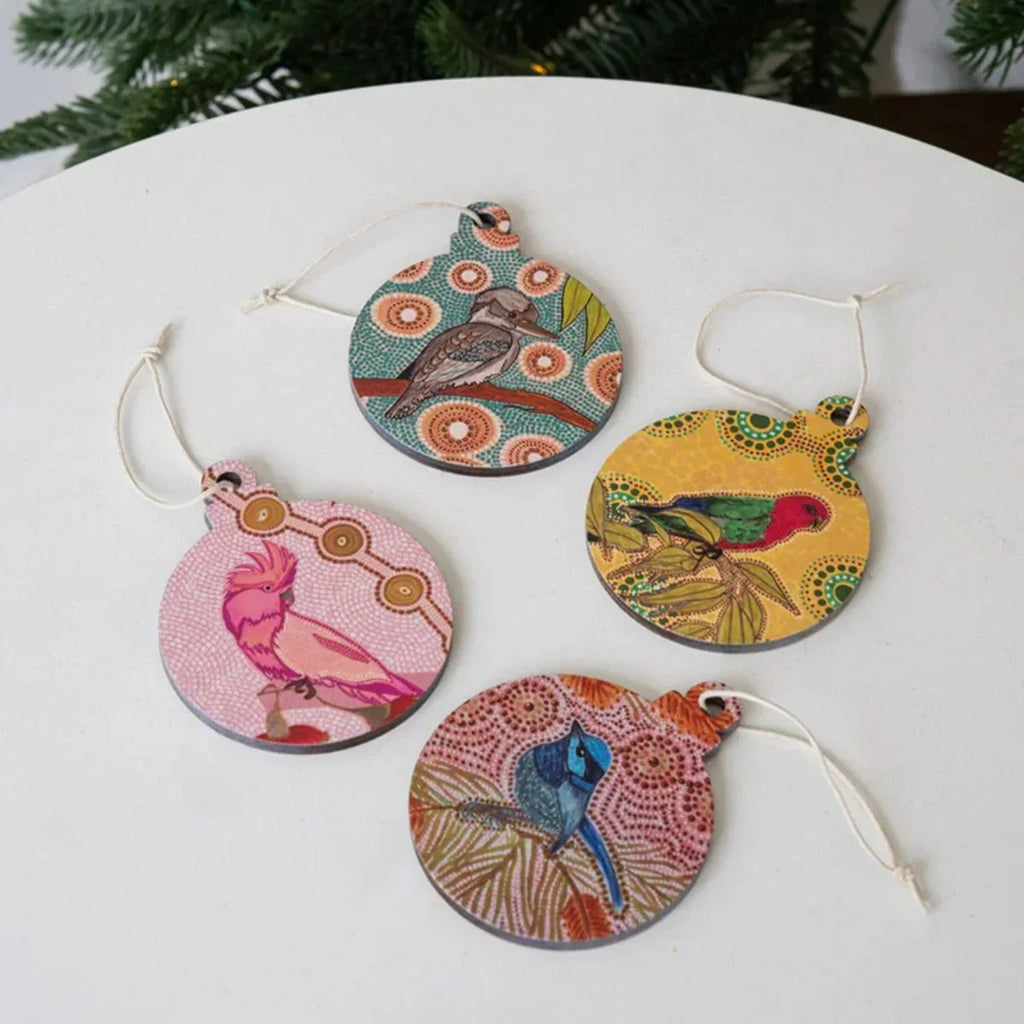 Four colorful bird-themed Christmas ornaments on a white surface with a blurred green background.