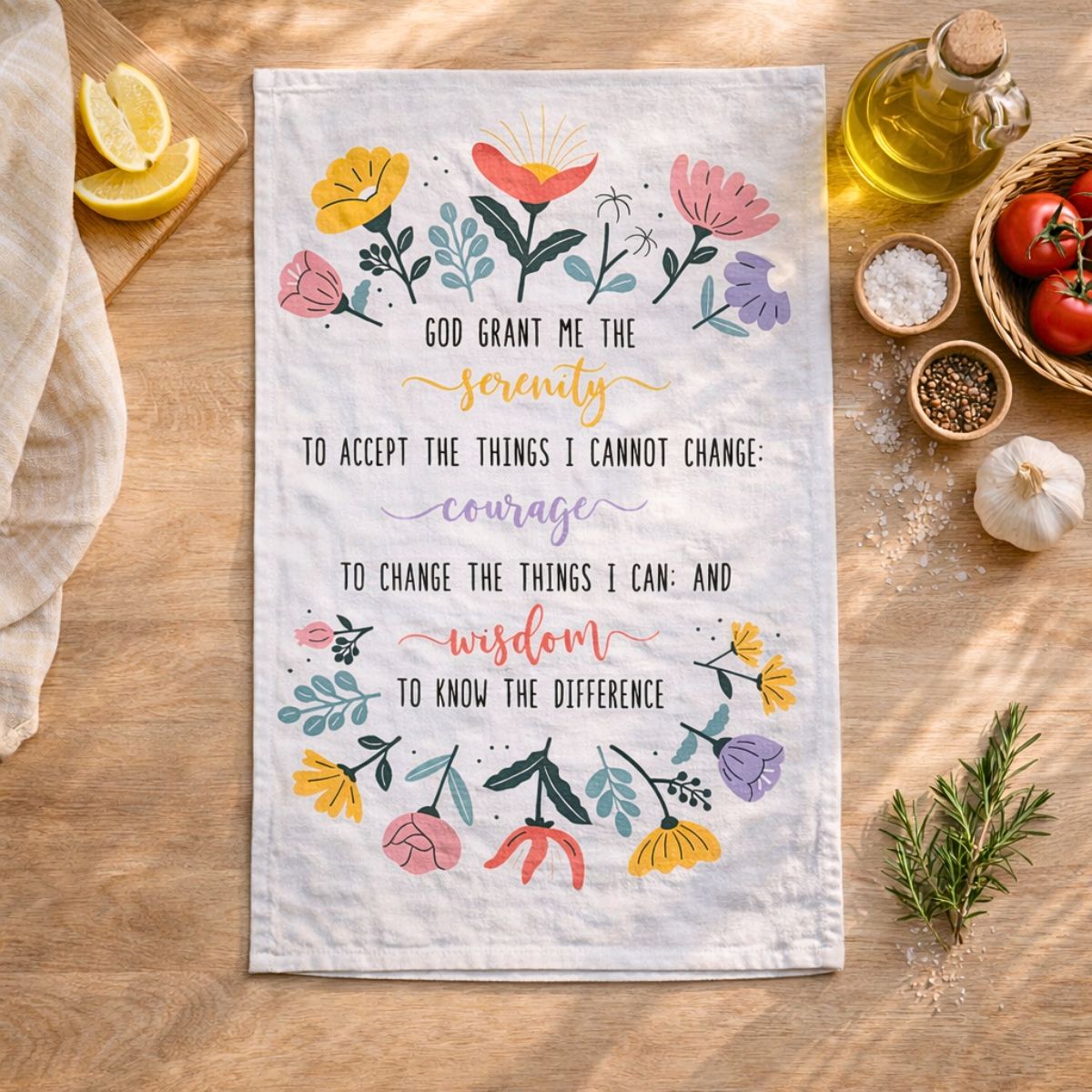 Tea towel with floral design and motivational quote on a wooden surface with kitchen items.