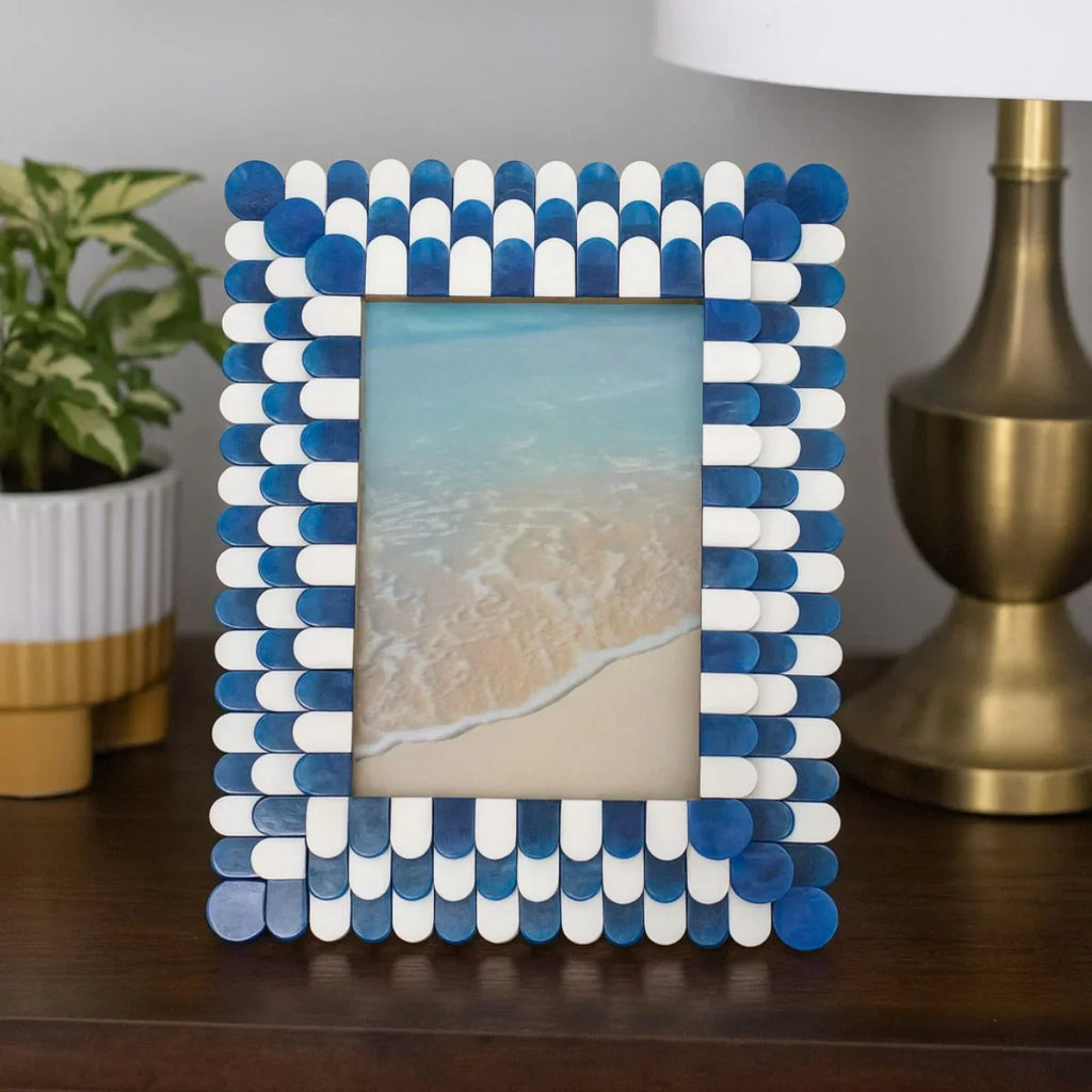 Blue and white picture frame on a table with a lamp and plant in the background