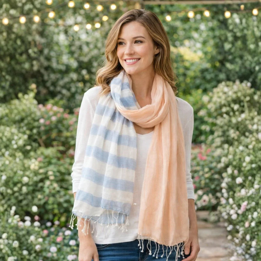 Woman wearing a striped scarf and a peach-colored scarf outdoors with greenery and flowers in the background