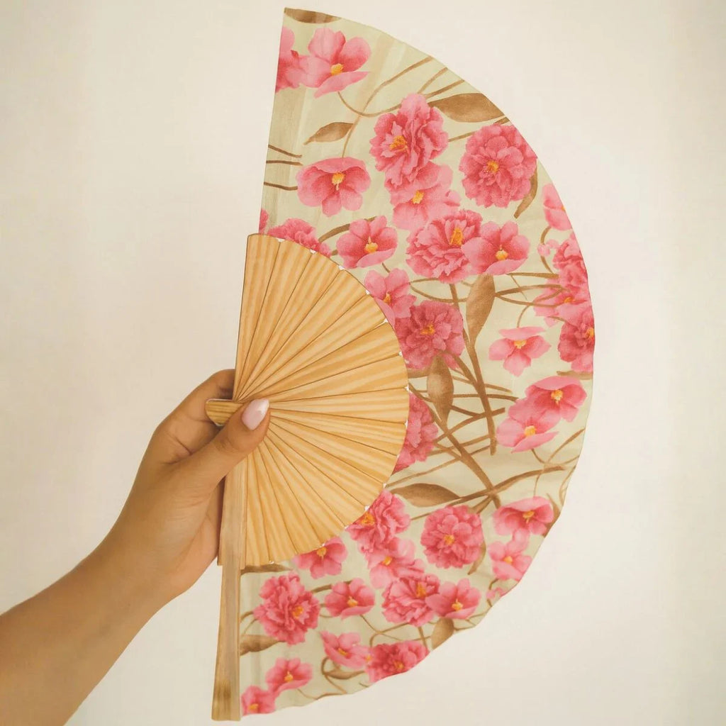 Hand holding a floral fan with pink flowers on a beige background