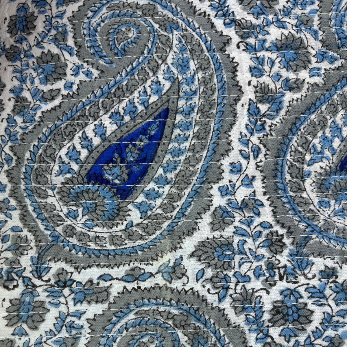 A close-up of a fabric or wallpaper pattern featuring a classic paisley design in blue, gray, and black on a white background.