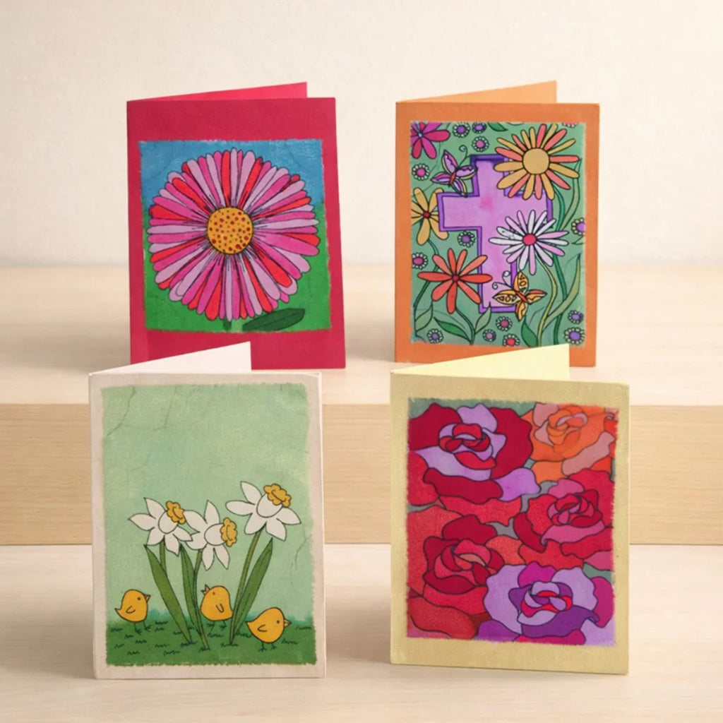 Four colorful greeting cards with floral designs on a wooden surface.