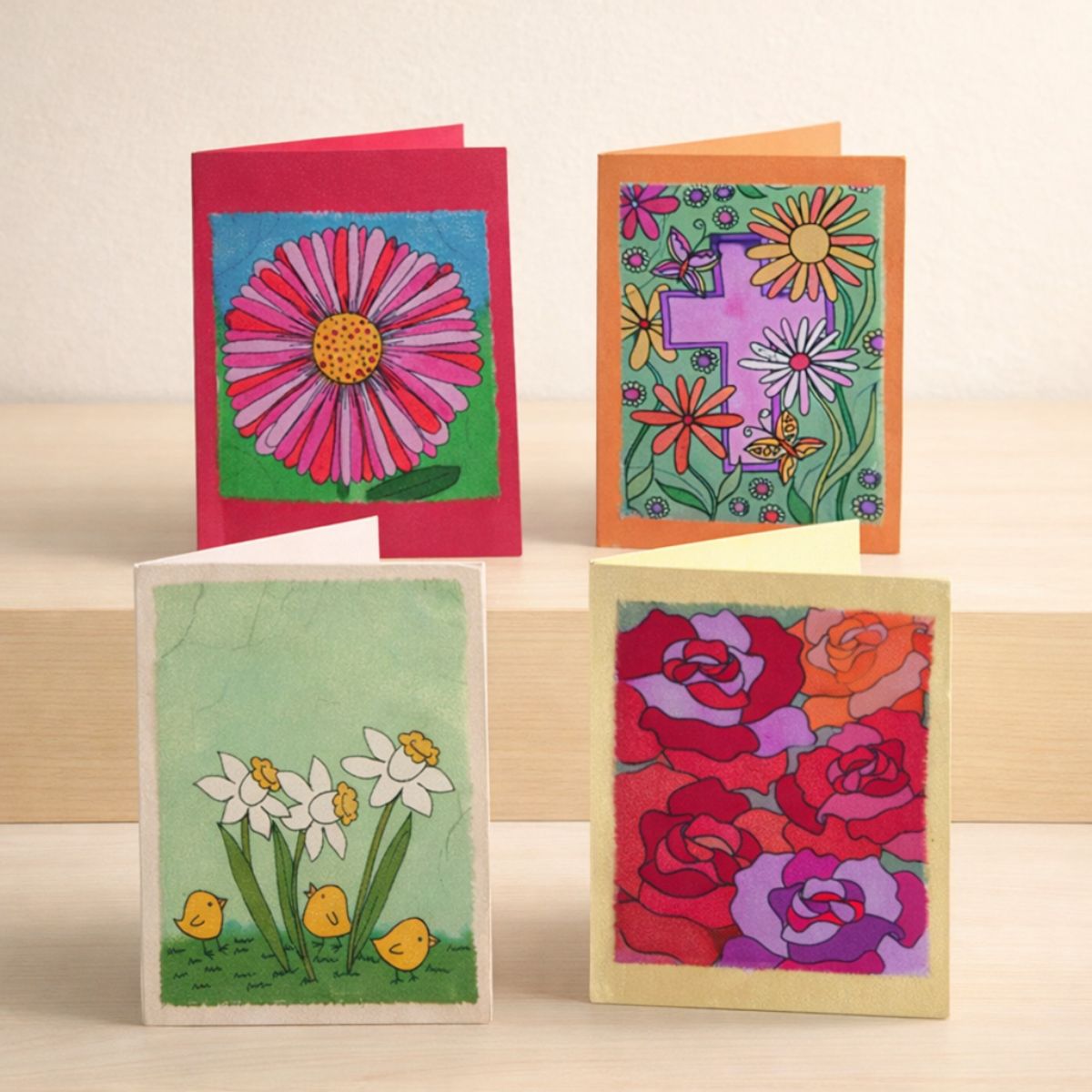 Four colorful greeting cards with floral designs on a wooden surface.