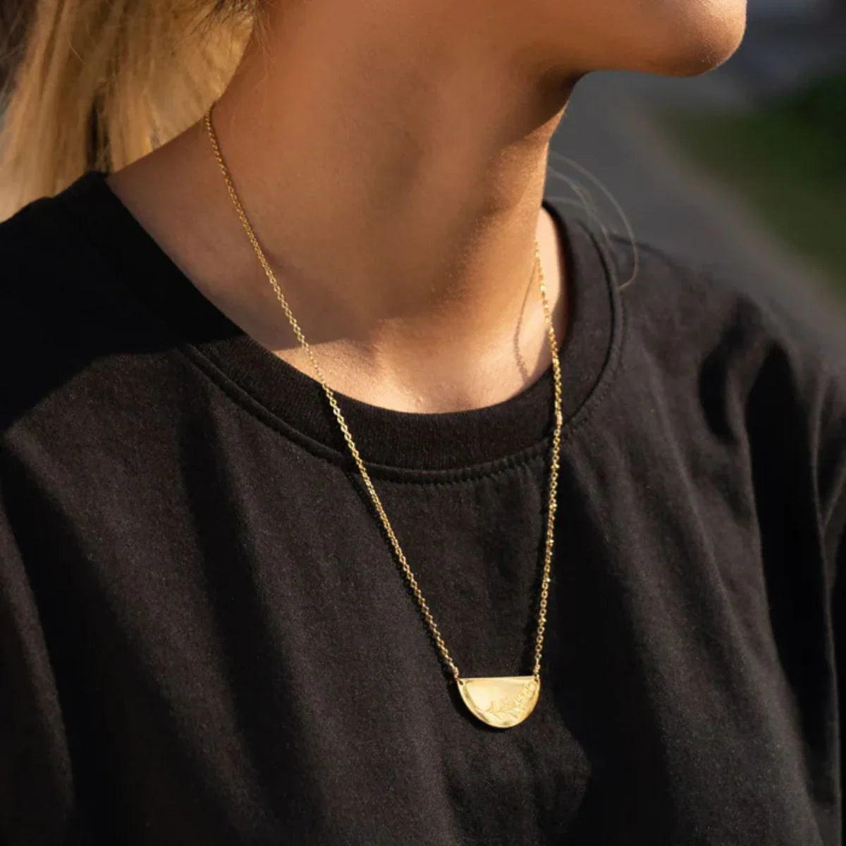 Person wearing a gold necklace with a black shirt against a blurred background