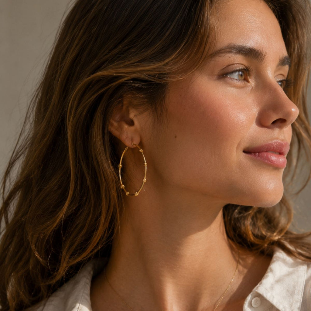 Close-up of a woman wearing gold hoop earrings with a neutral background